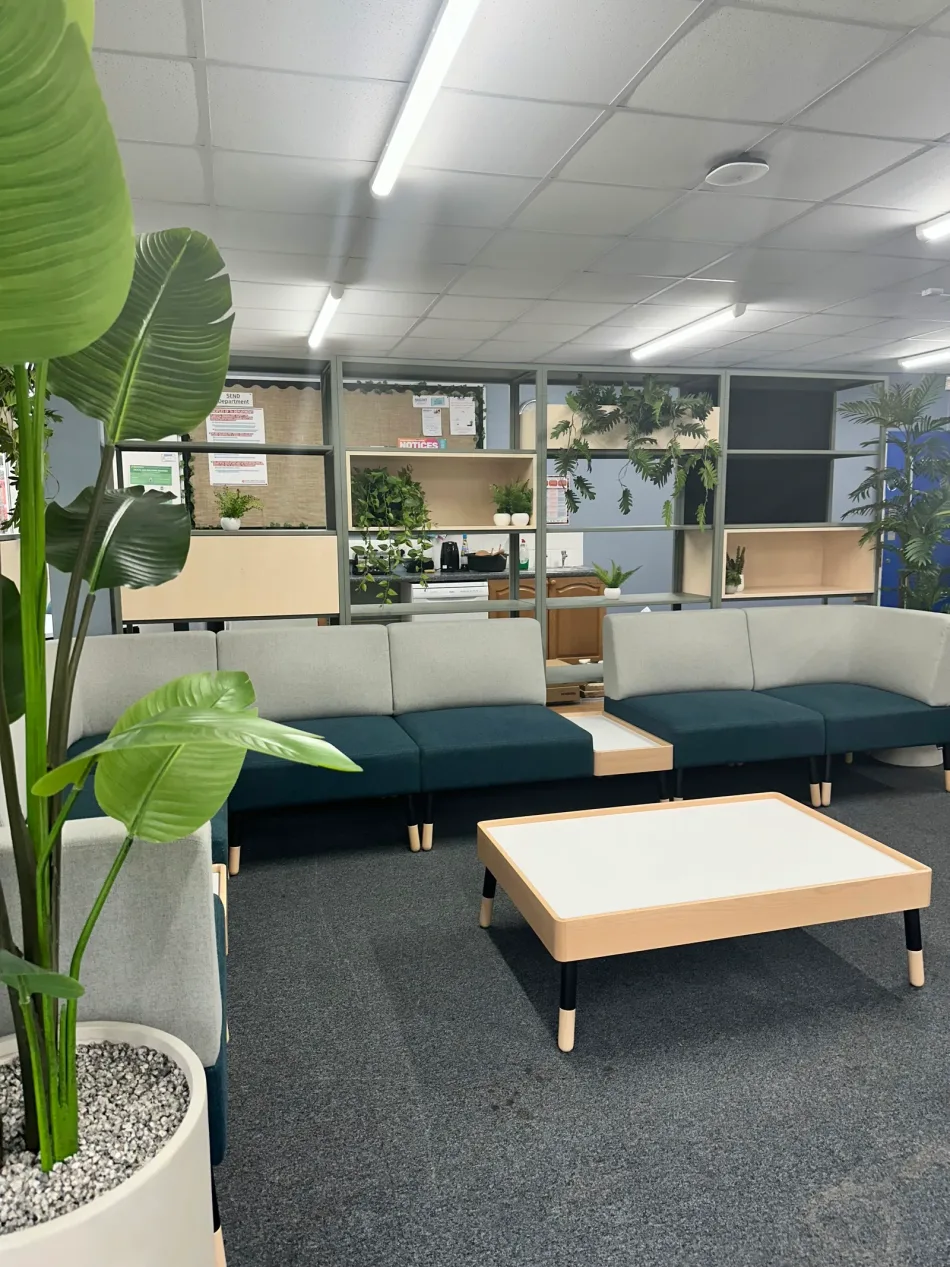 A calm breakout lounge with green and cream modular seating and planted shelving