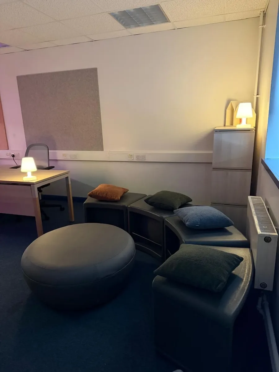 A quiet nurture room with soft seating, cushions and warm lamp lighting